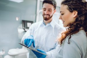 People, medicine, stomatology and health care concept – happy male dentist showing tablet pc computer to woman patient at dental clinic office.